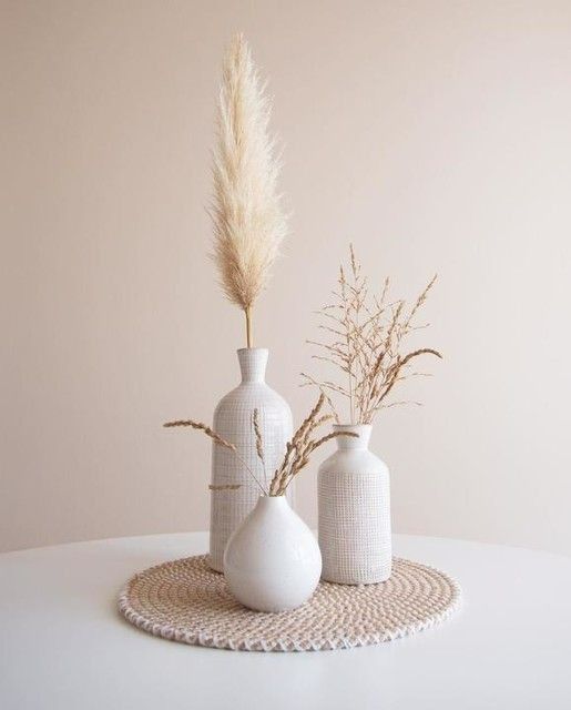 Set of ceramic vases with dried pampas and grass stems on woven mat, minimalist home décor accent piece