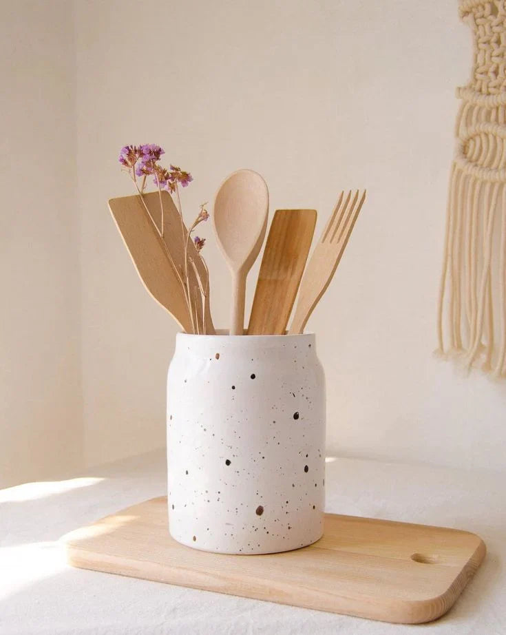 Speckled ceramic utensil holder with wooden spoons and fork on cutting board, modern kitchen decor accessory