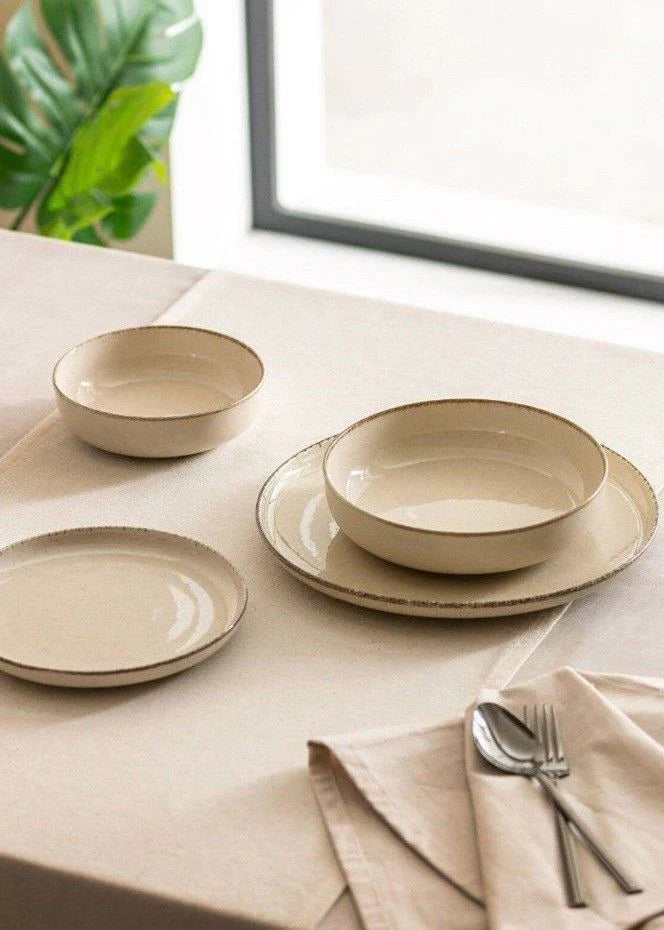 Beige ceramic dinnerware set with bowls and plates on linen tablecloth, minimalist dining table setup