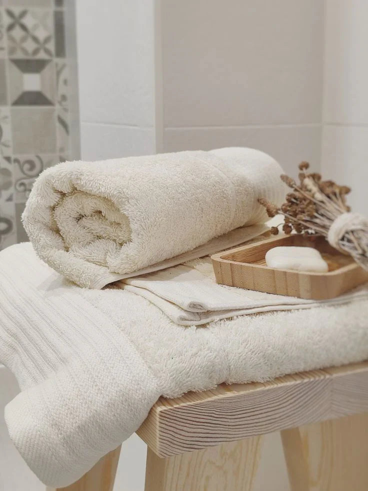 Soft beige bath towels with wooden soap dish and dried flowers on stool, minimalist spa-inspired bathroom decor
